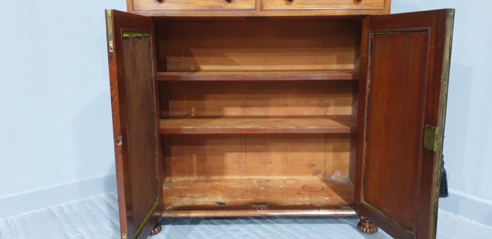 An antique Regency mahogany side cabinet featuring two top drawers over double doors with brass diamond grilles backed by green fabric, flanked by columns. View IX