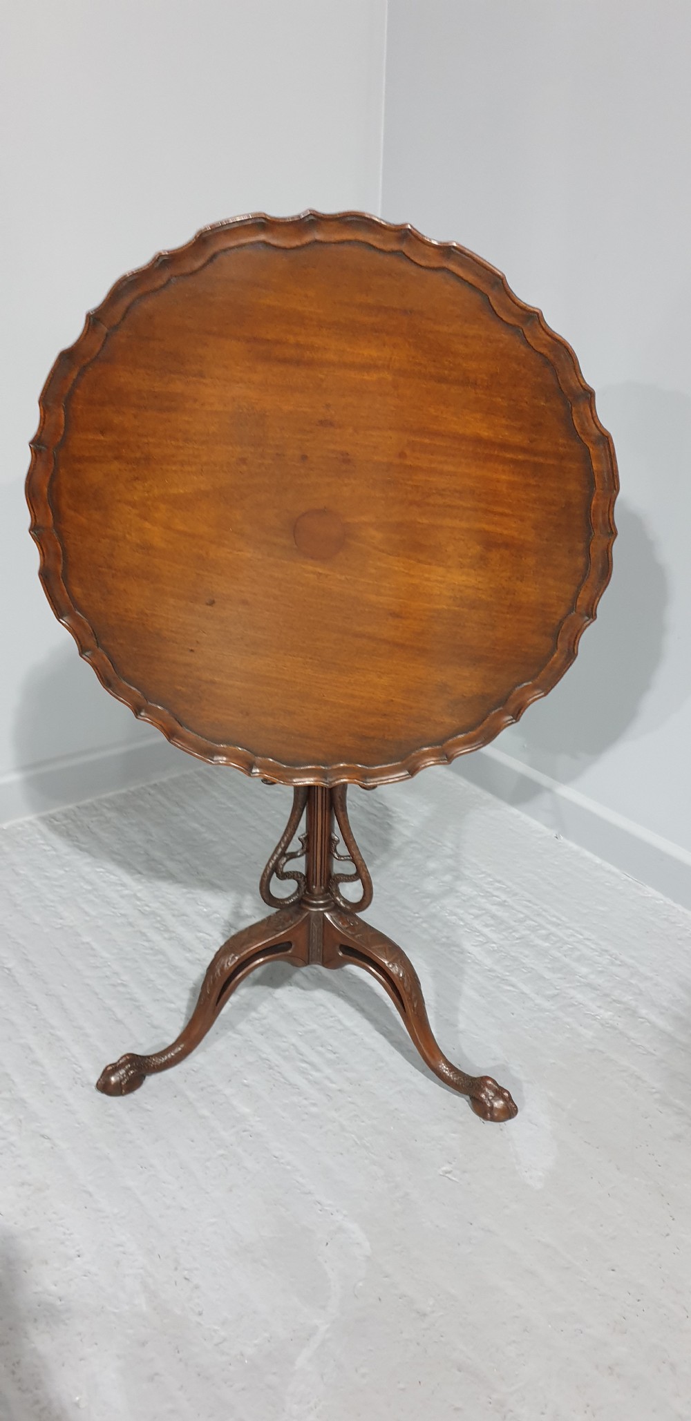 A mahogany tilt-top table with a pie-crust scalloped rim, resting on a carved tripod base with cabriole legs.