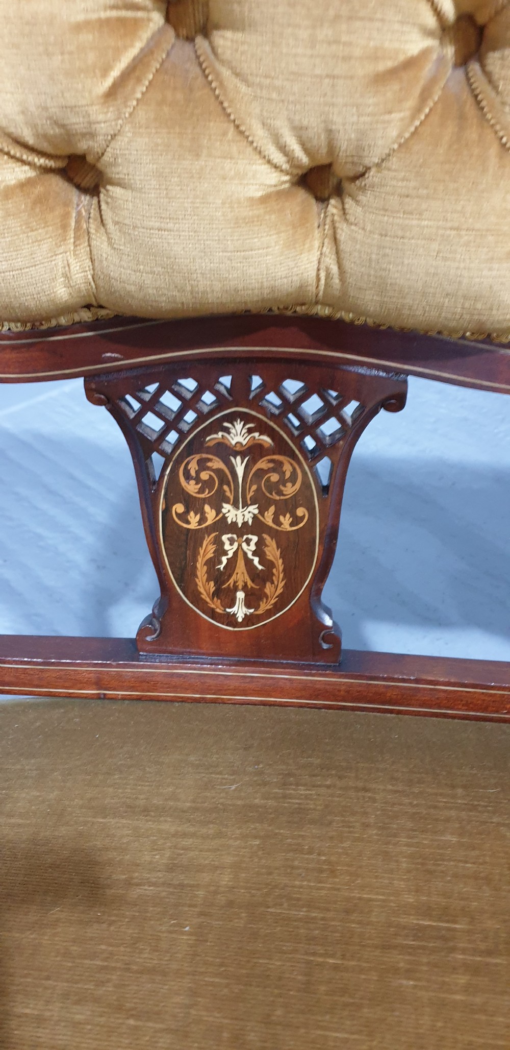 An Edwardian mahogany two-seat settee upholstered in button-tufted gold velvet with decorative marquetry inlays on the backrest and arm supports. View V
