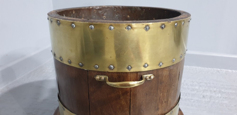 A cylindrical mahogany wood log bin with wide polished brass bands and side carrying handles. View IV