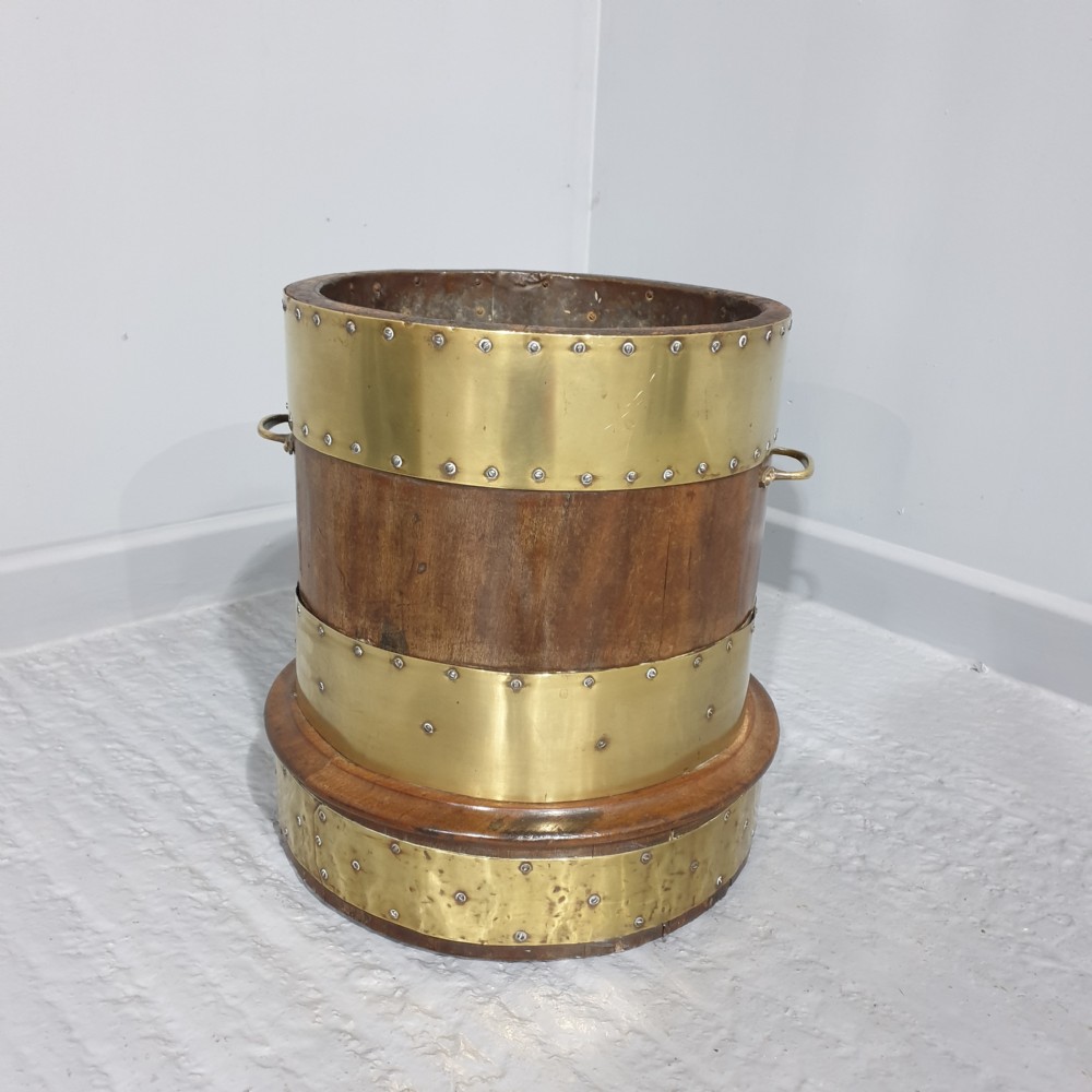 A cylindrical mahogany wood log bin with wide polished brass bands and side carrying handles.