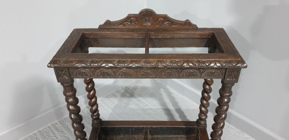 A dark oak stick stand with carved top cresting, barley twist support legs, carved frieze, and lower drip tray. View II