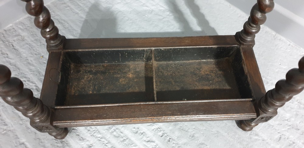 A dark oak stick stand with carved top cresting, barley twist support legs, carved frieze, and lower drip tray. View V