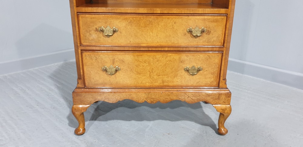 A low burr walnut open bookcase featuring a top shelf filled with leather-bound books, two lower drawers with brass handles, and cabriole legs. View VI