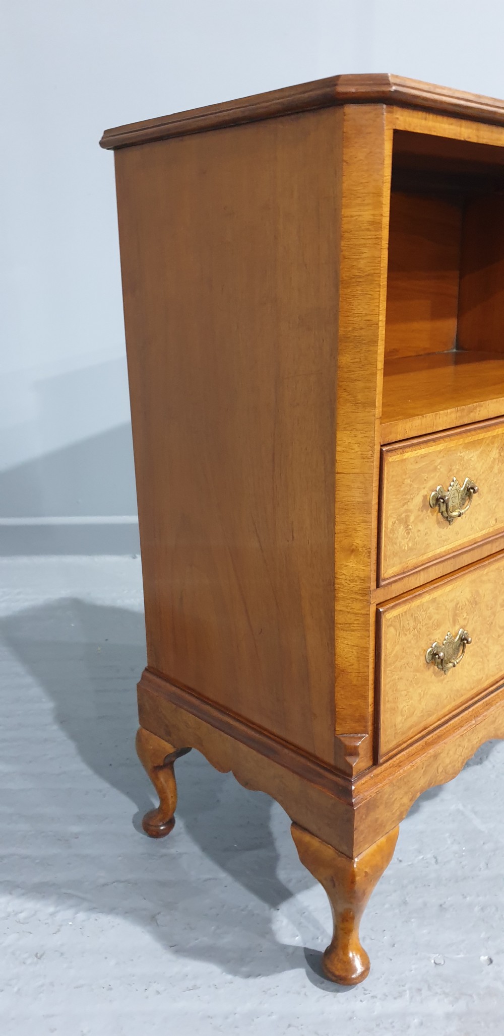 A low burr walnut open bookcase featuring a top shelf filled with leather-bound books, two lower drawers with brass handles, and cabriole legs. View X