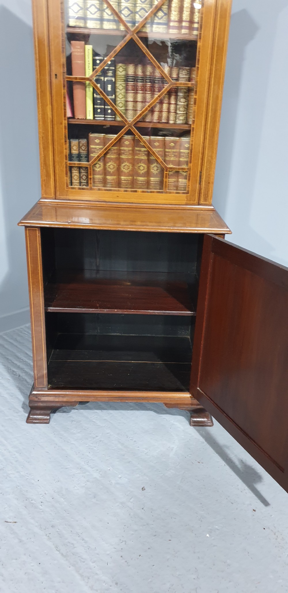 A narrow mahogany standing bookcase featuring a swan-neck pediment top, geometric astragal glazed door, and a lower door with an inlaid oval shell cartouche. View VII