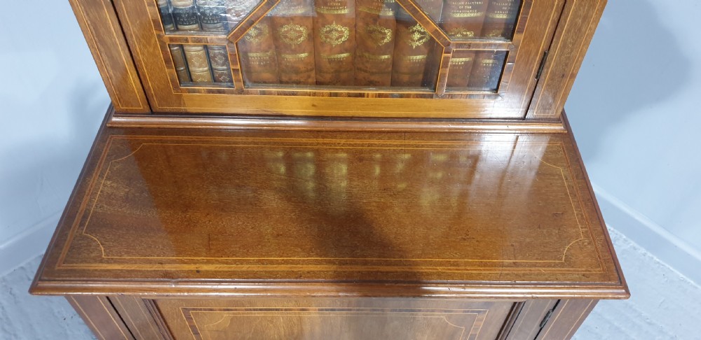 A narrow mahogany standing bookcase featuring a swan-neck pediment top, geometric astragal glazed door, and a lower door with an inlaid oval shell cartouche. View X