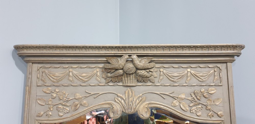 A French grey painted overmantel mirror featuring a carved dove frieze, floral swags, and an arched gilded frame. View III