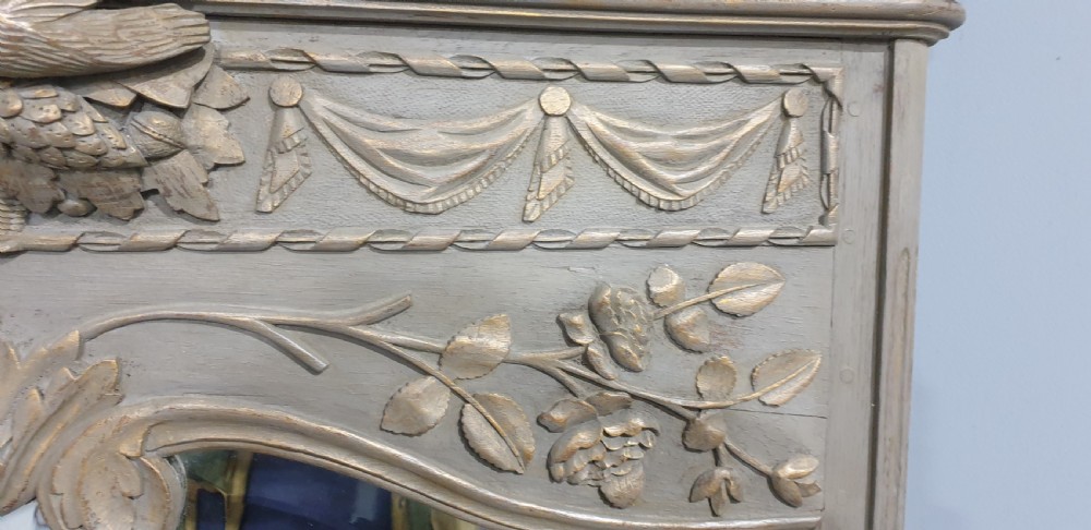 A French grey painted overmantel mirror featuring a carved dove frieze, floral swags, and an arched gilded frame. View V