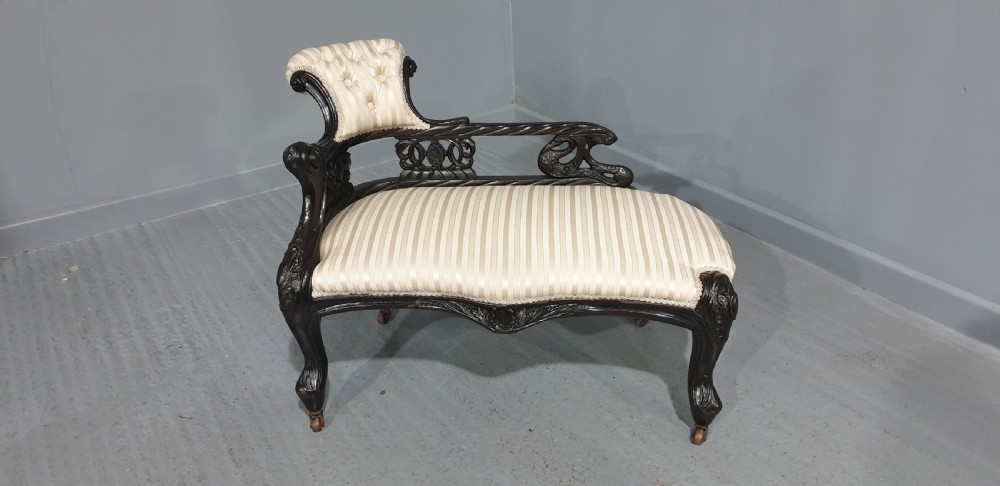 An ebonised wooden miniature chaise longue featuring a button-tufted backrest, cream striped fabric seat, carved frame, and cabriole legs on brass castors. View II