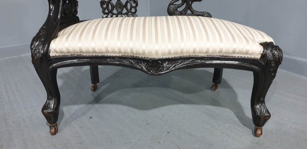 An ebonised wooden miniature chaise longue featuring a button-tufted backrest, cream striped fabric seat, carved frame, and cabriole legs on brass castors. View III