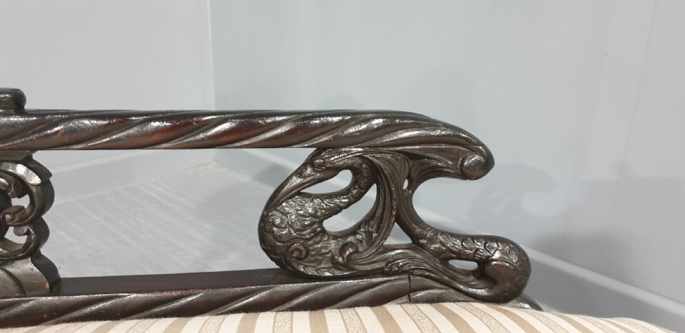 An ebonised wooden miniature chaise longue featuring a button-tufted backrest, cream striped fabric seat, carved frame, and cabriole legs on brass castors. View V