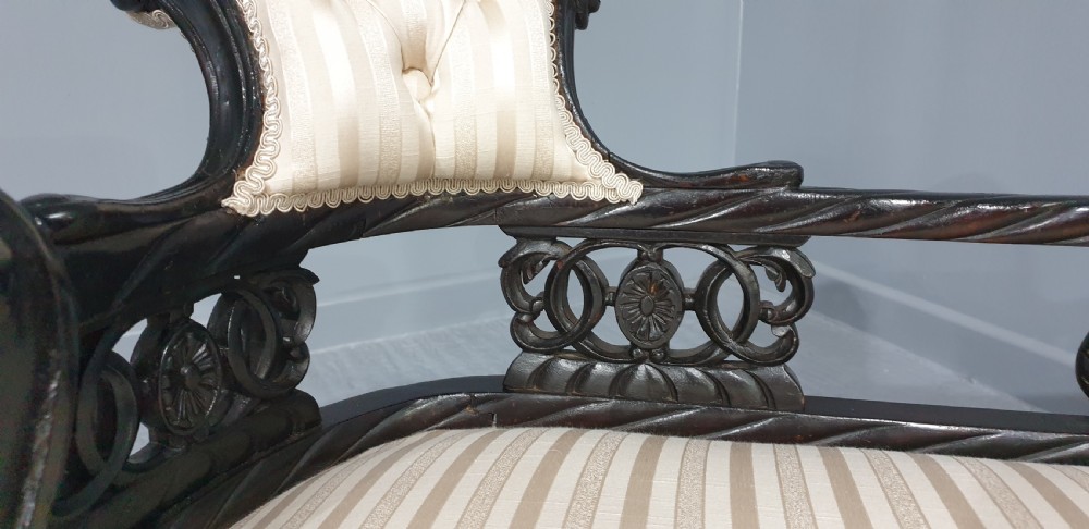 An ebonised wooden miniature chaise longue featuring a button-tufted backrest, cream striped fabric seat, carved frame, and cabriole legs on brass castors. View VI