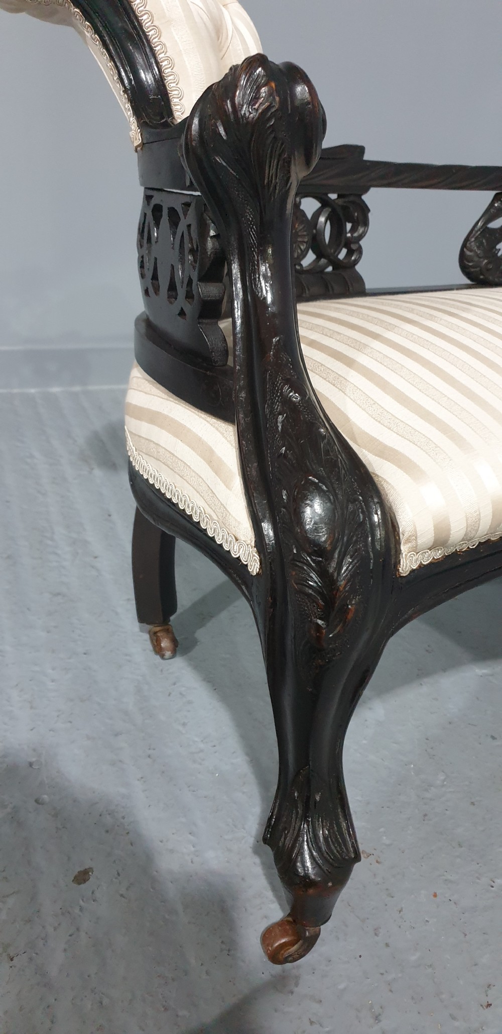 An ebonised wooden miniature chaise longue featuring a button-tufted backrest, cream striped fabric seat, carved frame, and cabriole legs on brass castors. View VII