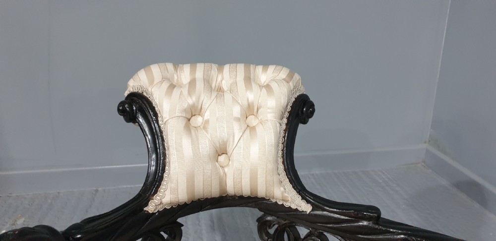 An ebonised wooden miniature chaise longue featuring a button-tufted backrest, cream striped fabric seat, carved frame, and cabriole legs on brass castors. View VIII