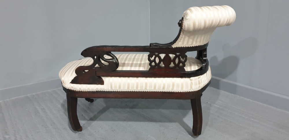 An ebonised wooden miniature chaise longue featuring a button-tufted backrest, cream striped fabric seat, carved frame, and cabriole legs on brass castors. View IX