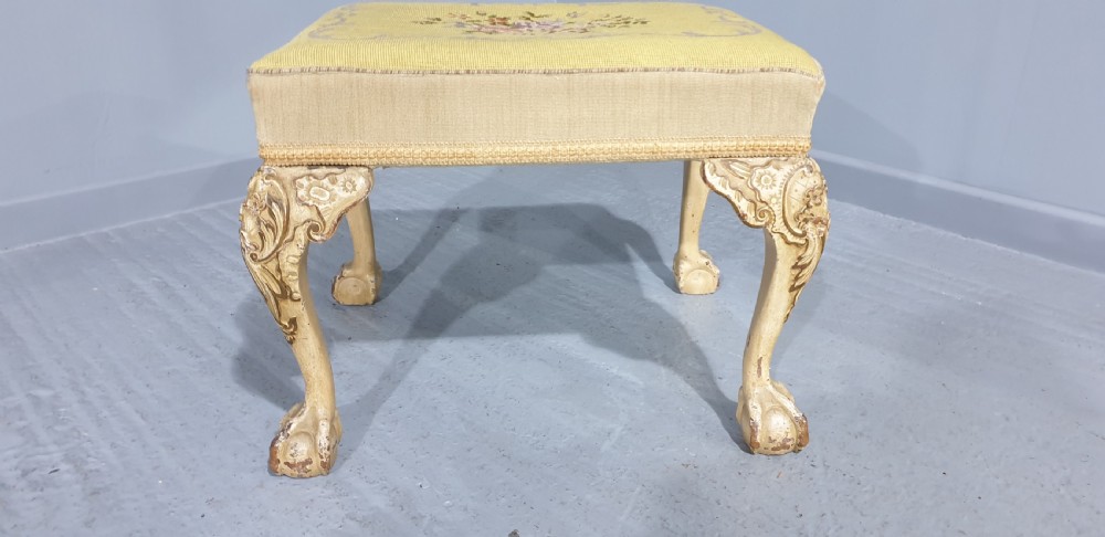 A low rectangular antique stool featuring cream painted cabriole legs with carved knees, ball and claw feet, and a yellow floral needlepoint seat. View II