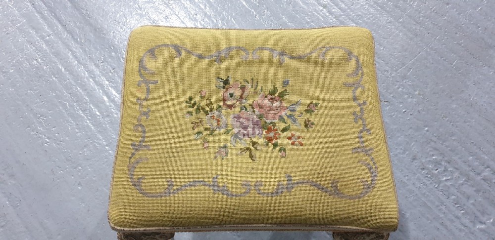 A low rectangular antique stool featuring cream painted cabriole legs with carved knees, ball and claw feet, and a yellow floral needlepoint seat. View V