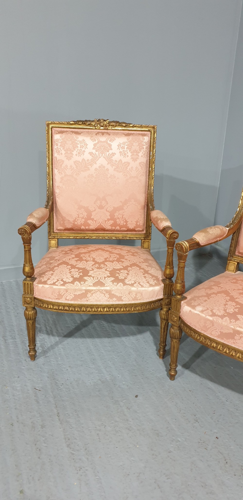 A pair of French Louis XVI style giltwood fauteuil armchairs with fluted legs, carved crests, and pink damask pattern upholstery. View II