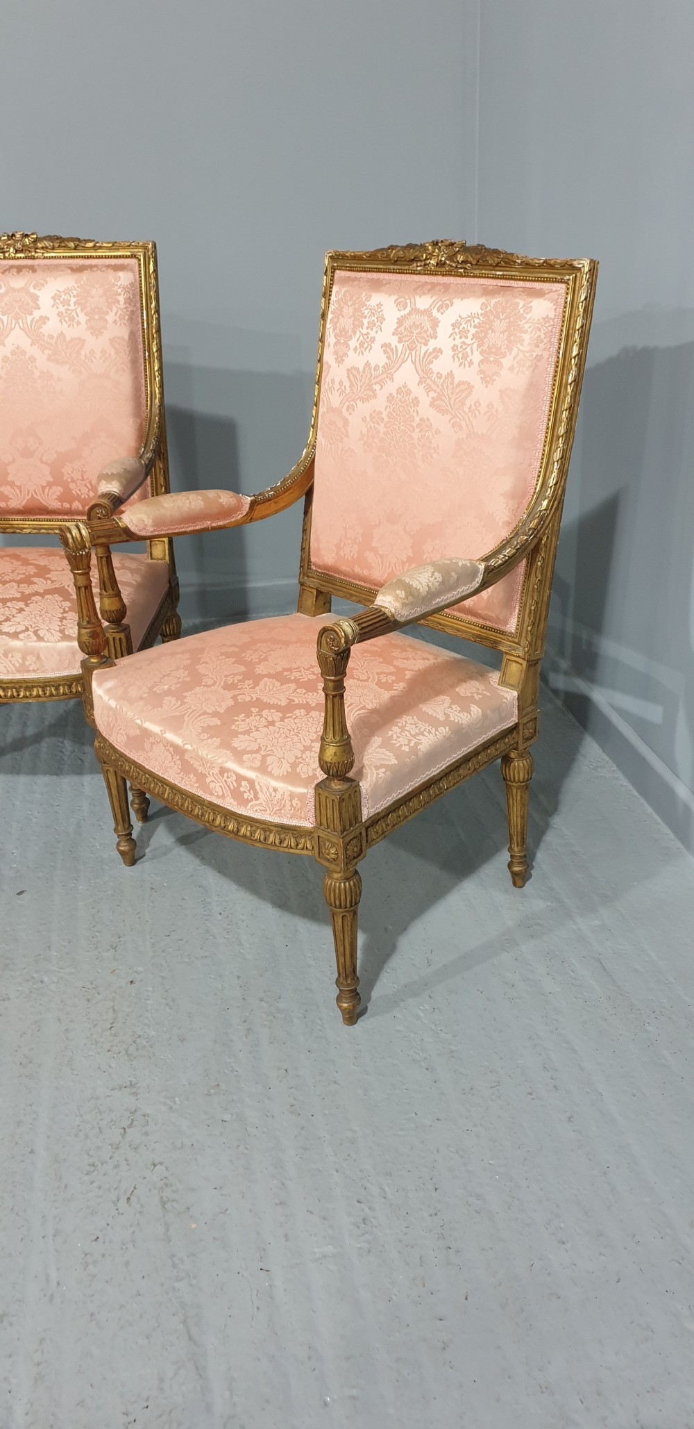 A pair of French Louis XVI style giltwood fauteuil armchairs with fluted legs, carved crests, and pink damask pattern upholstery. View III