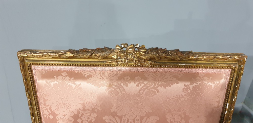 A pair of French Louis XVI style giltwood fauteuil armchairs with fluted legs, carved crests, and pink damask pattern upholstery. View V