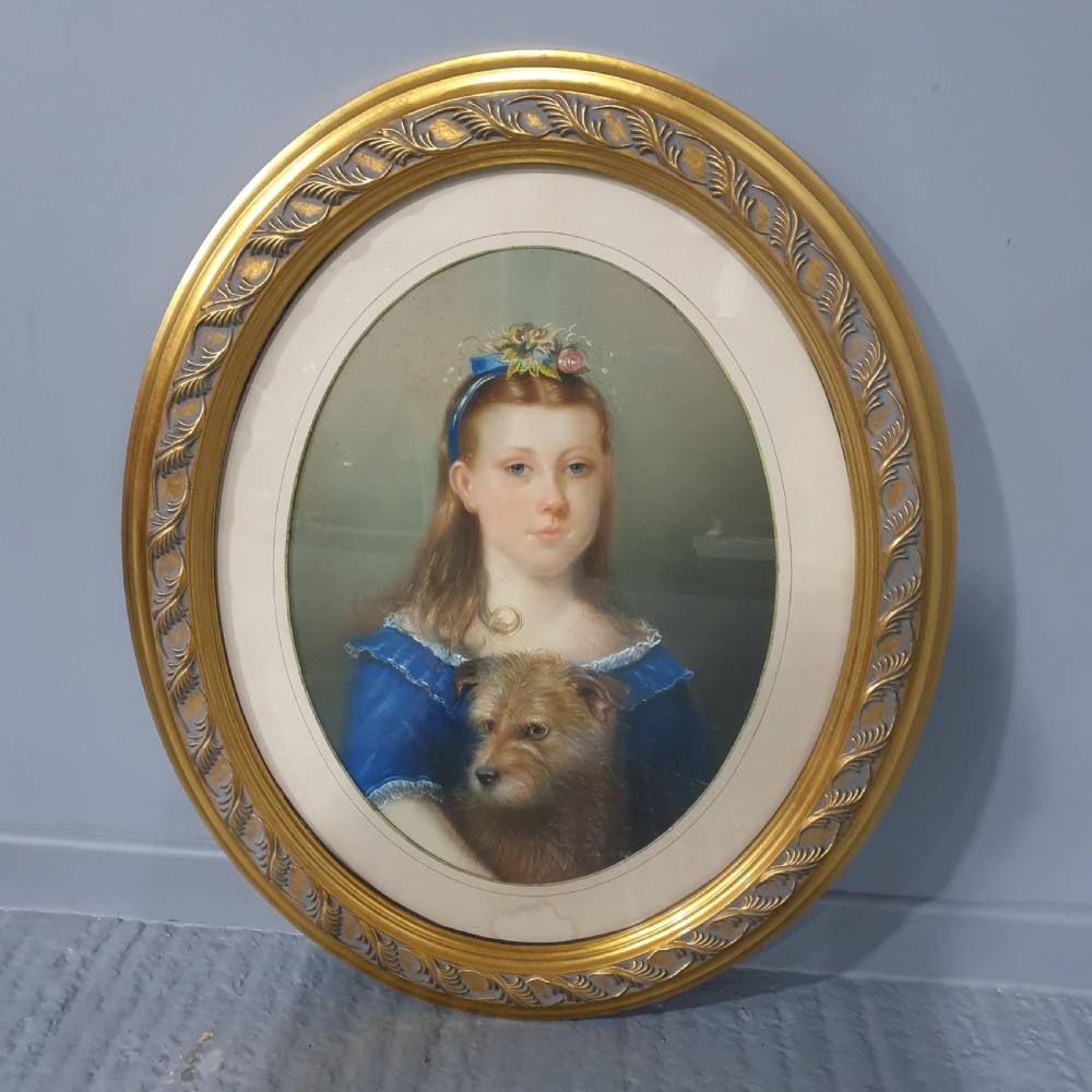 An antique oval Victorian portrait depicting a young girl in a blue dress holding a small dog, set within a carved gold gilded frame.