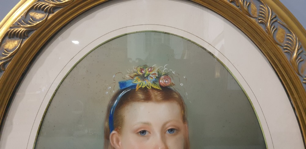 An antique oval Victorian portrait depicting a young girl in a blue dress holding a small dog, set within a carved gold gilded frame. View II