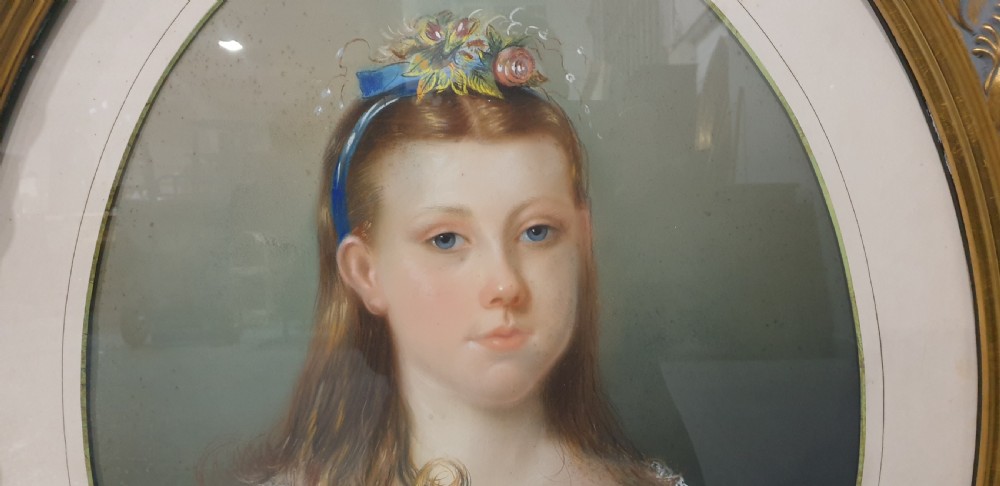 An antique oval Victorian portrait depicting a young girl in a blue dress holding a small dog, set within a carved gold gilded frame. View III