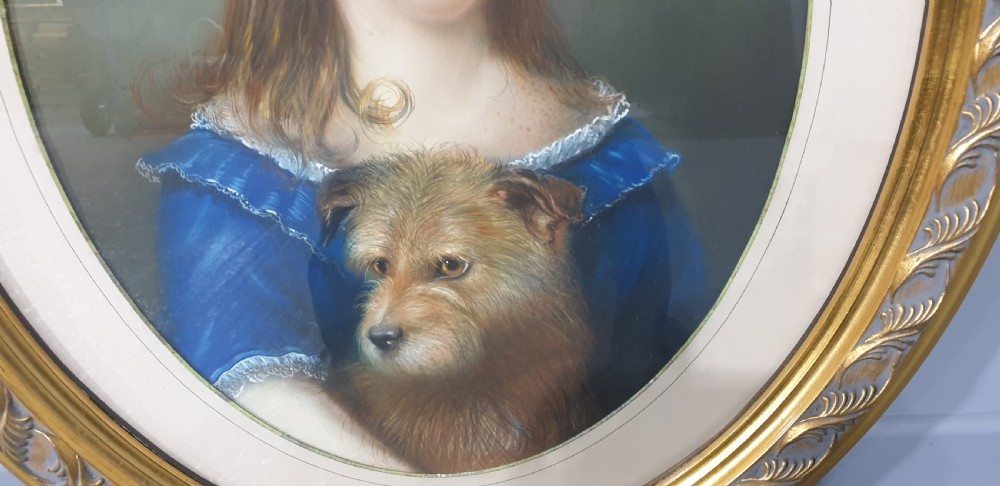 An antique oval Victorian portrait depicting a young girl in a blue dress holding a small dog, set within a carved gold gilded frame. View IV