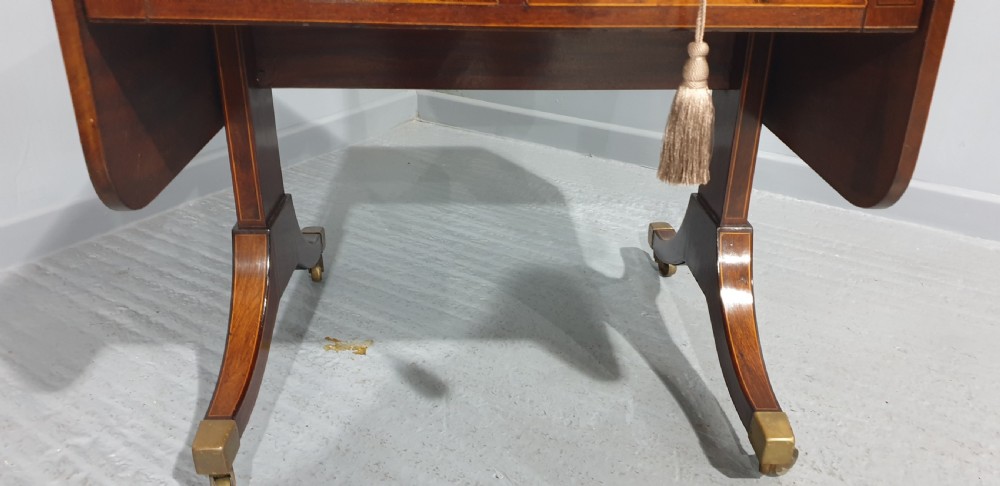 An 18th-century mahogany drop-leaf sofa table with two frieze drawers, crossbanded inlay, sabre legs, and brass castors. View V