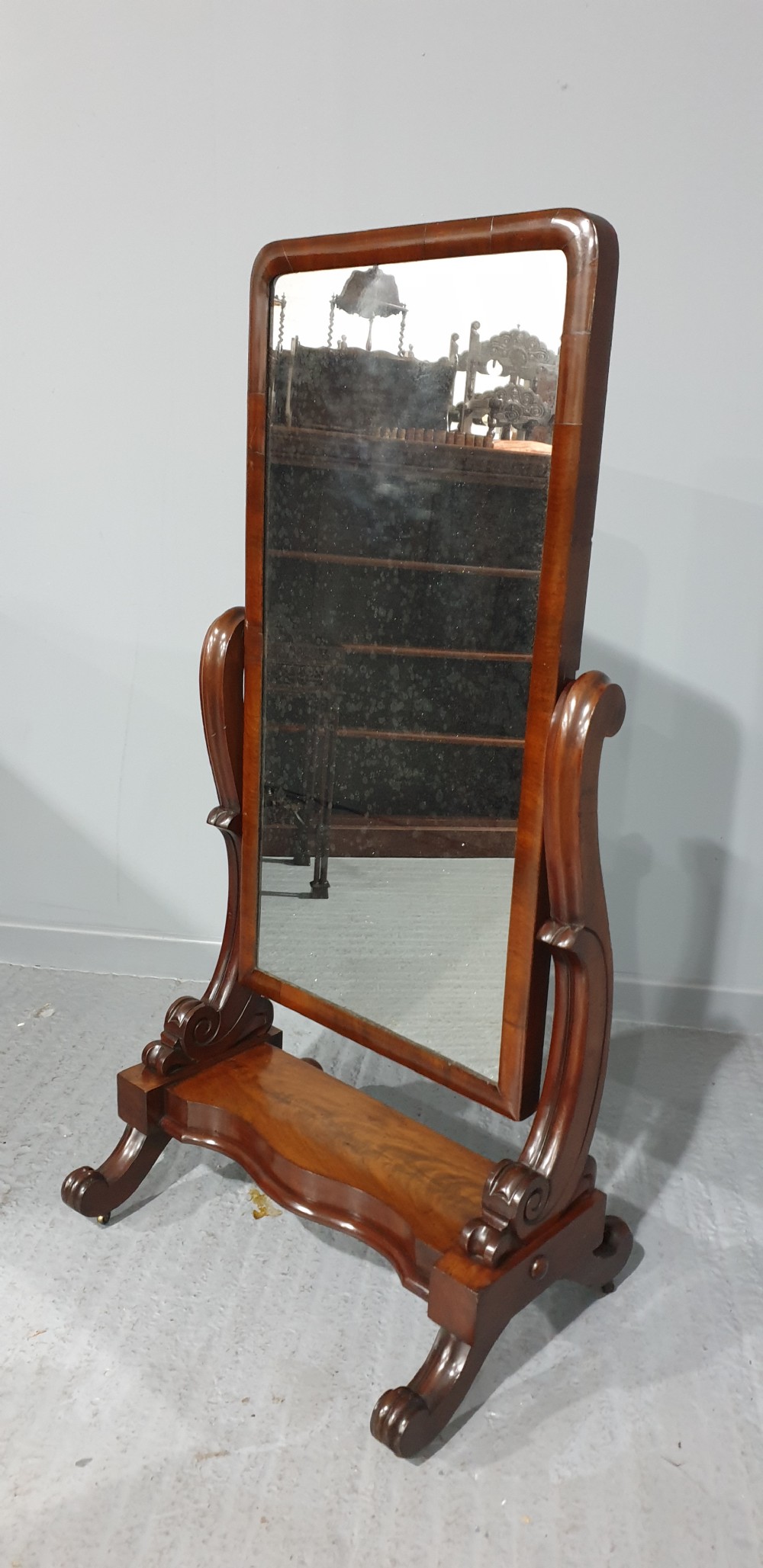 A Victorian mahogany freestanding cheval mirror featuring a rounded rectangular tilting frame on carved scroll legs and a plinth base. View III