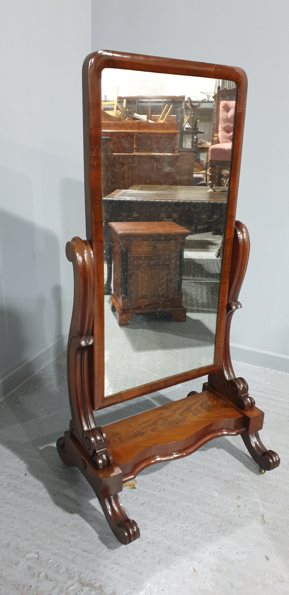 A Victorian mahogany freestanding cheval mirror featuring a rounded rectangular tilting frame on carved scroll legs and a plinth base. View IV
