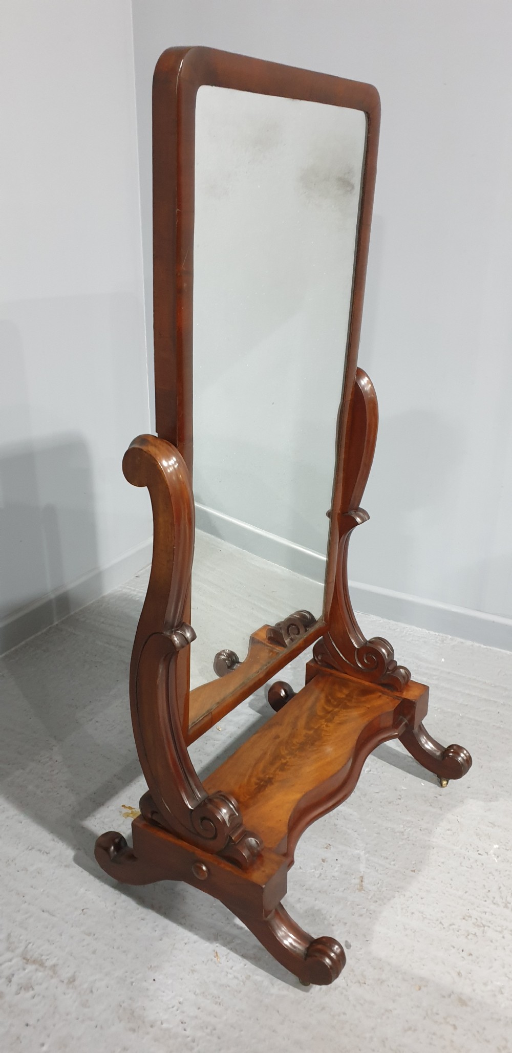 A Victorian mahogany freestanding cheval mirror featuring a rounded rectangular tilting frame on carved scroll legs and a plinth base. View IX