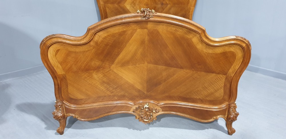 A French Louis XV style walnut bed frame featuring quarter-matched veneered panels and parcel gilt hand-carved cresting on the headboard and footboard. View II