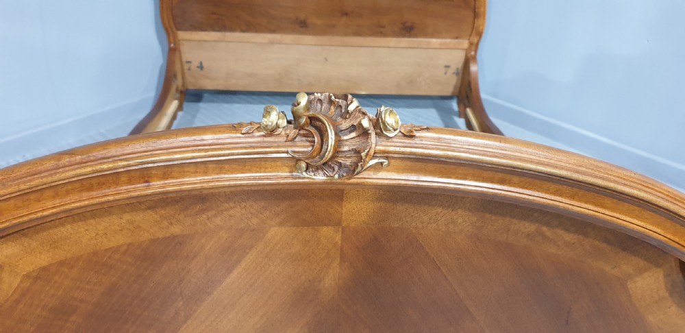 A French Louis XV style walnut bed frame featuring quarter-matched veneered panels and parcel gilt hand-carved cresting on the headboard and footboard. View V
