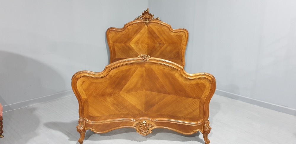 A French Louis XV style walnut bed frame featuring quarter-matched veneered panels and parcel gilt hand-carved cresting on the headboard and footboard. View XV
