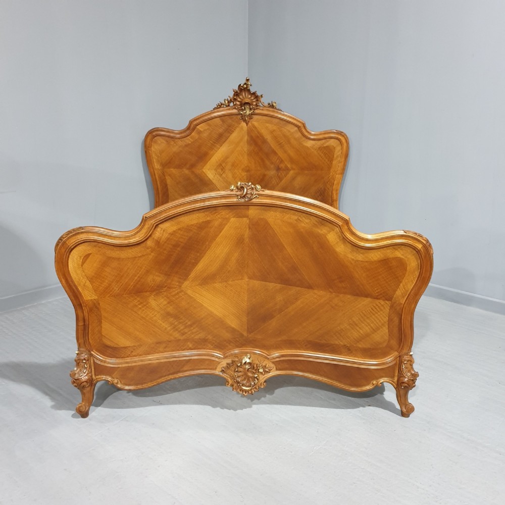 A French Louis XV style walnut bed frame featuring quarter-matched veneered panels and parcel gilt hand-carved cresting on the headboard and footboard.