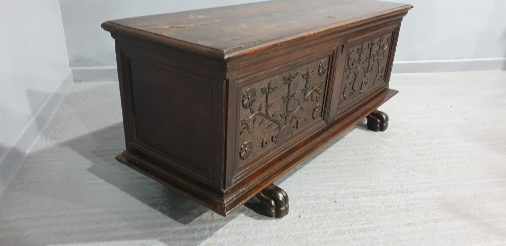 A dark brown carved wood Italian cassone coffer featuring two foliate relief panels and carved lion paw feet. View VI
