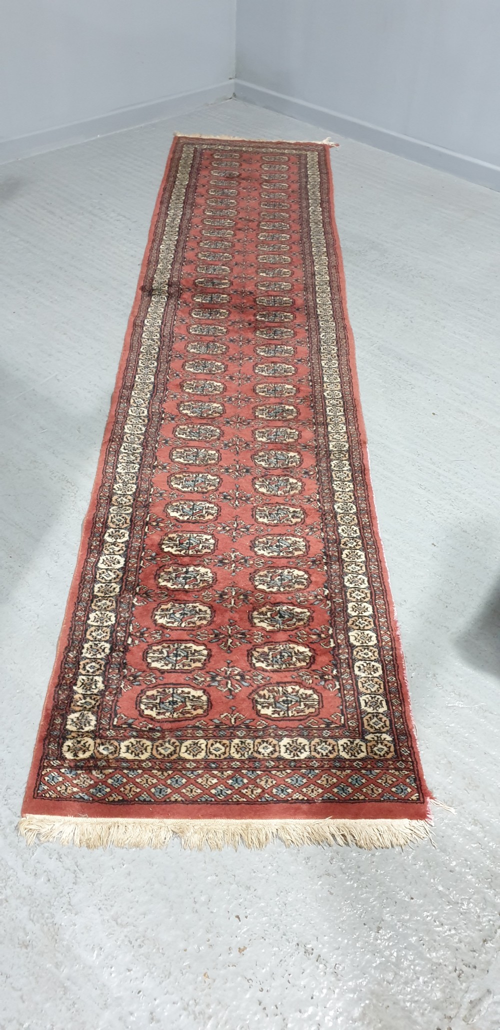 An extra-long hand-knotted wool carpet runner featuring repeated geometric medallion patterns on a terracotta red field with patterned cream borders. View II