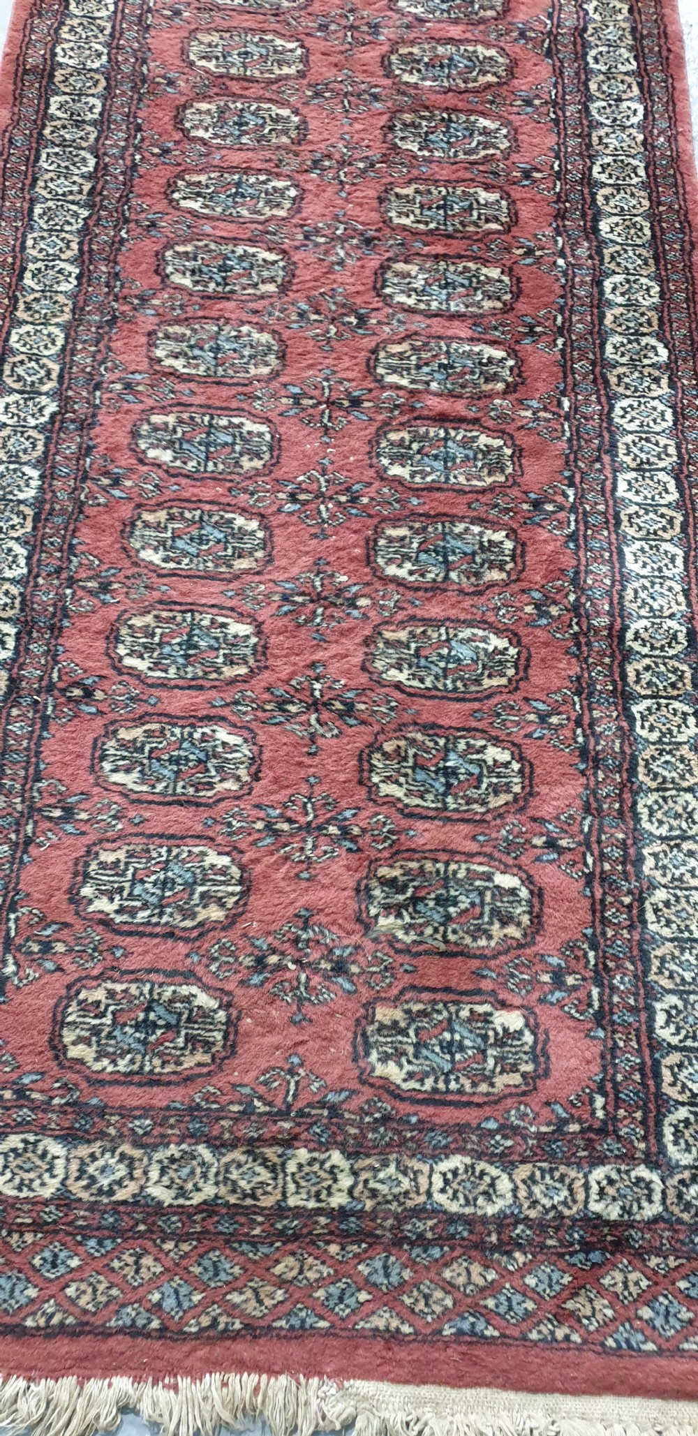 An extra-long hand-knotted wool carpet runner featuring repeated geometric medallion patterns on a terracotta red field with patterned cream borders. View VIII