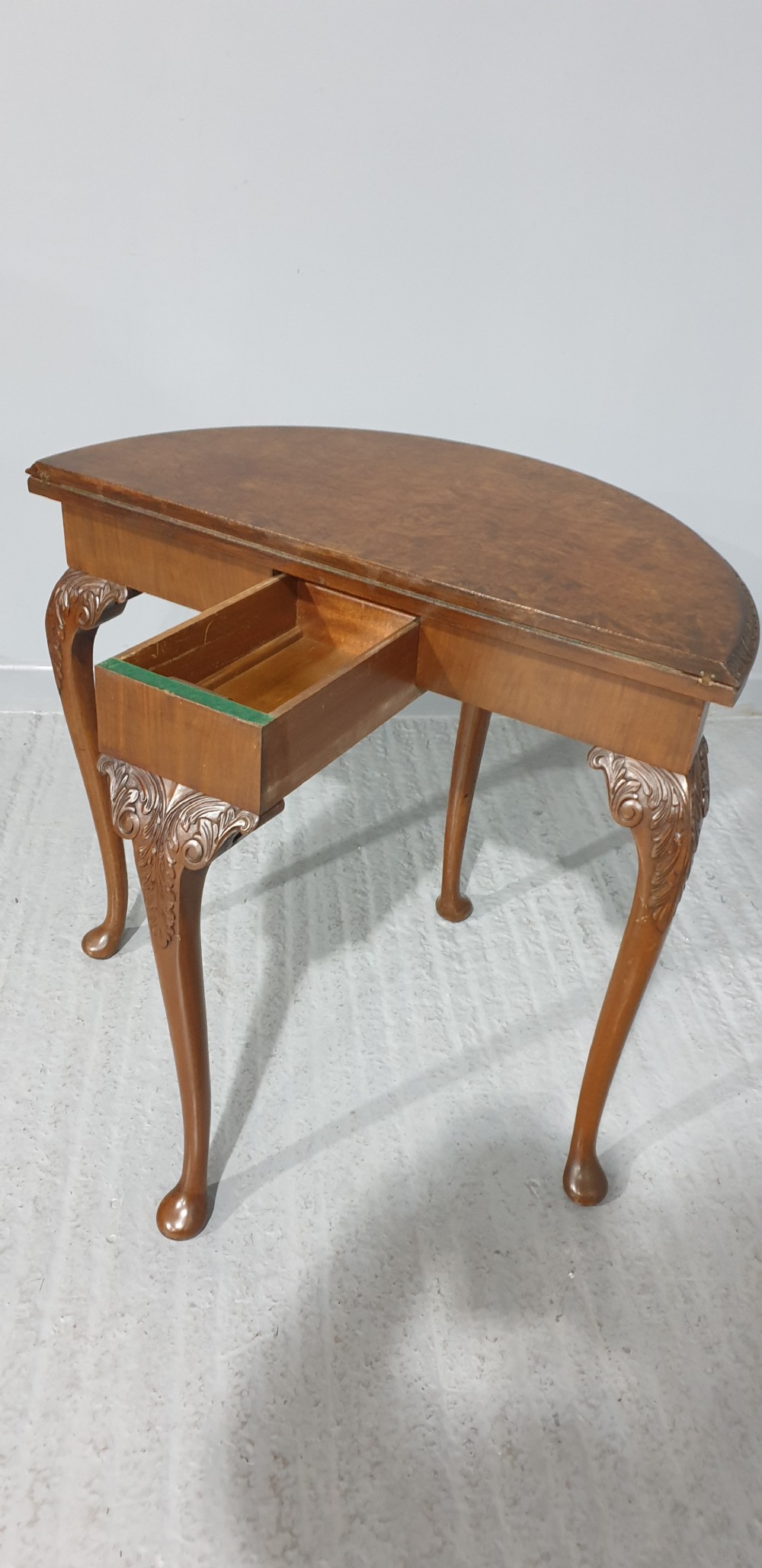A semi-circular burr walnut games table with a fold-over top, carved edge moulding, and cabriole legs featuring carved knees and pad feet. View V