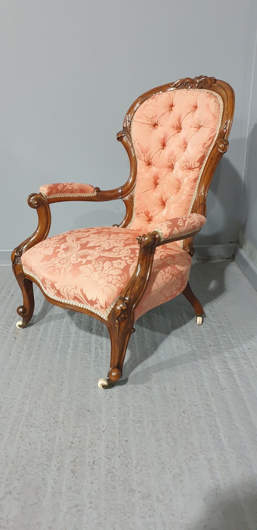 A Victorian carved mahogany armchair featuring button-tufted peach damask upholstery, scroll arms, and cabriole legs with castors. View III