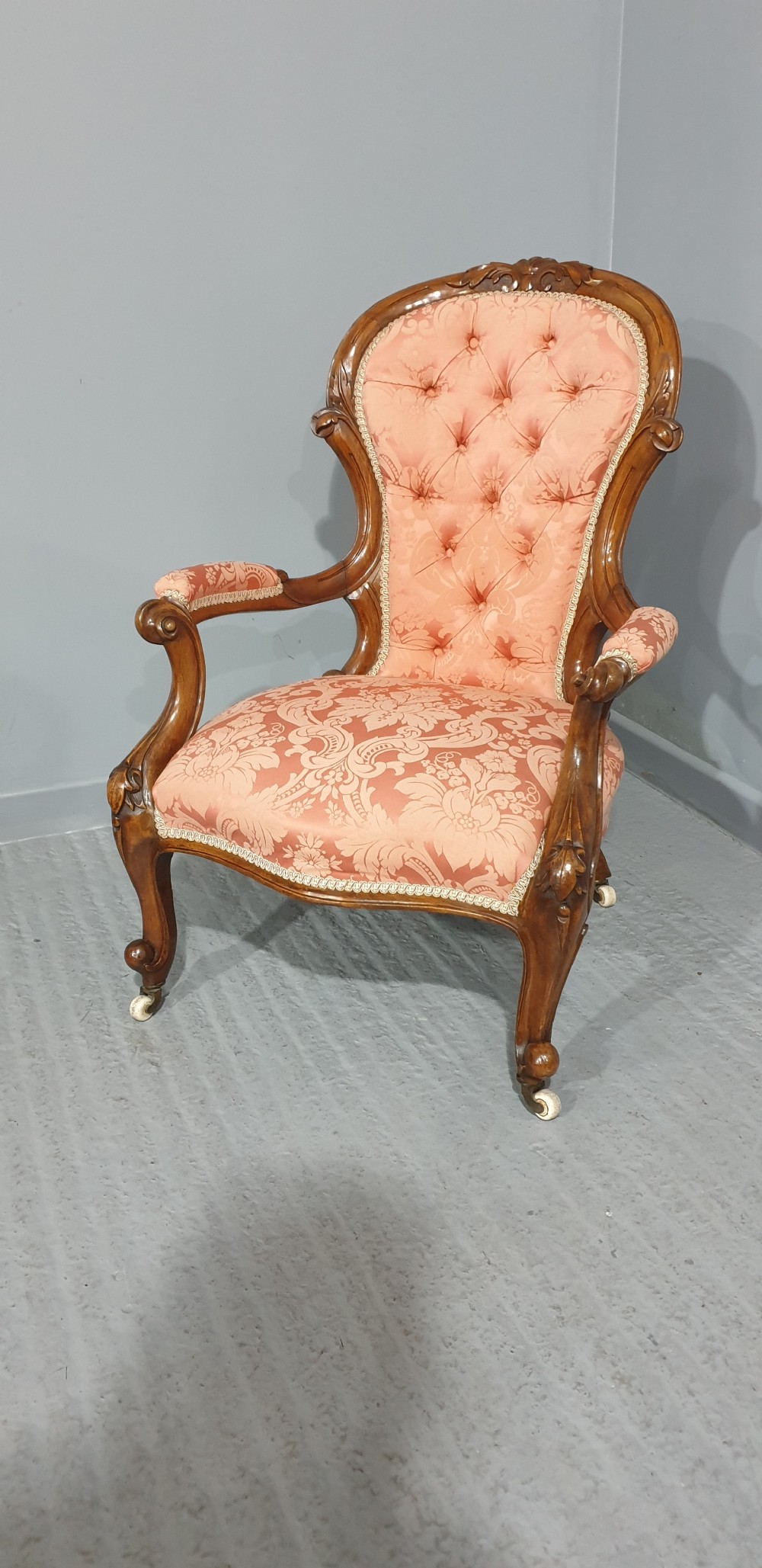 A Victorian carved mahogany armchair featuring button-tufted peach damask upholstery, scroll arms, and cabriole legs with castors. View IV