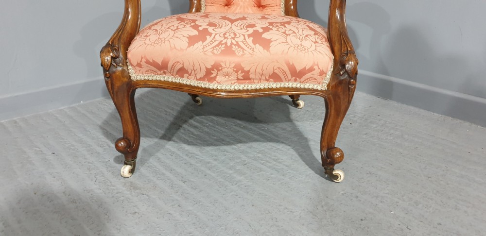A Victorian carved mahogany armchair featuring button-tufted peach damask upholstery, scroll arms, and cabriole legs with castors. View V