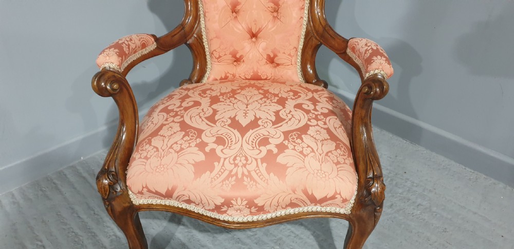 A Victorian carved mahogany armchair featuring button-tufted peach damask upholstery, scroll arms, and cabriole legs with castors. View VI