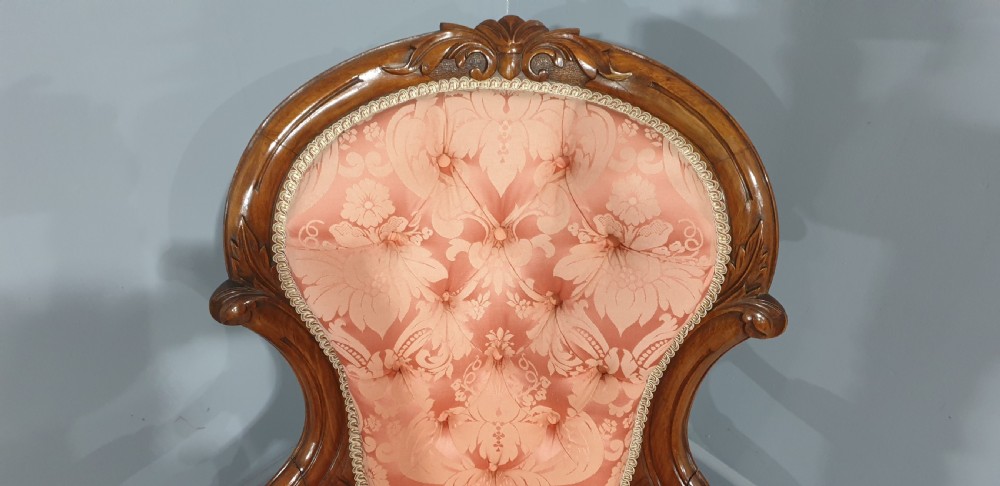 A Victorian carved mahogany armchair featuring button-tufted peach damask upholstery, scroll arms, and cabriole legs with castors. View VII