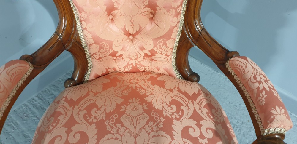 A Victorian carved mahogany armchair featuring button-tufted peach damask upholstery, scroll arms, and cabriole legs with castors. View VIII