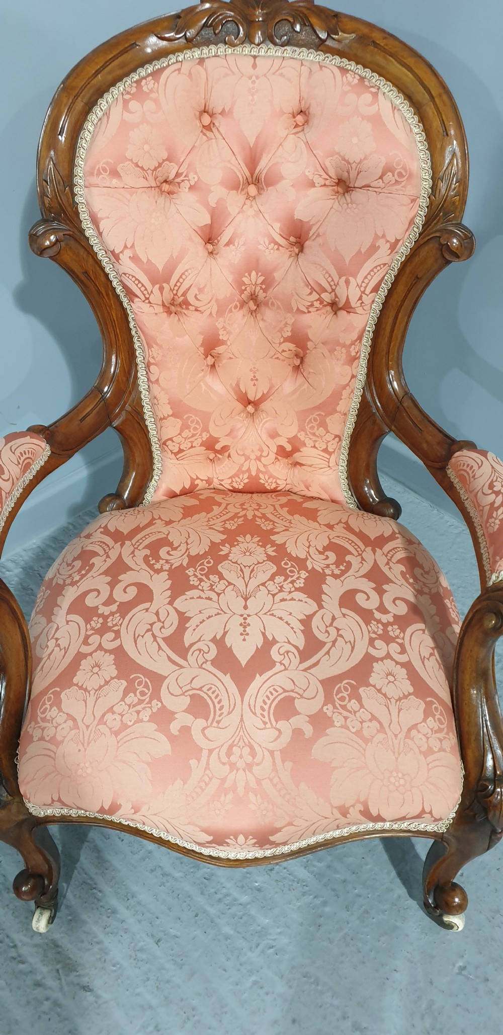 A Victorian carved mahogany armchair featuring button-tufted peach damask upholstery, scroll arms, and cabriole legs with castors. View IX