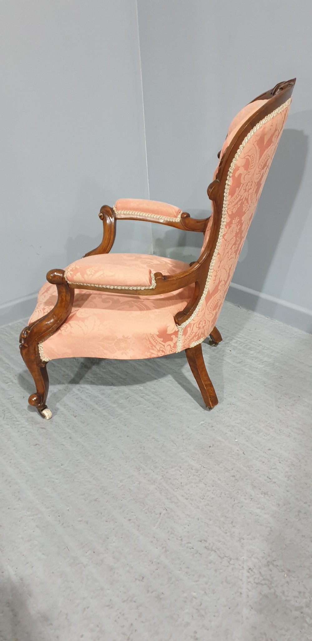 A Victorian carved mahogany armchair featuring button-tufted peach damask upholstery, scroll arms, and cabriole legs with castors. View X