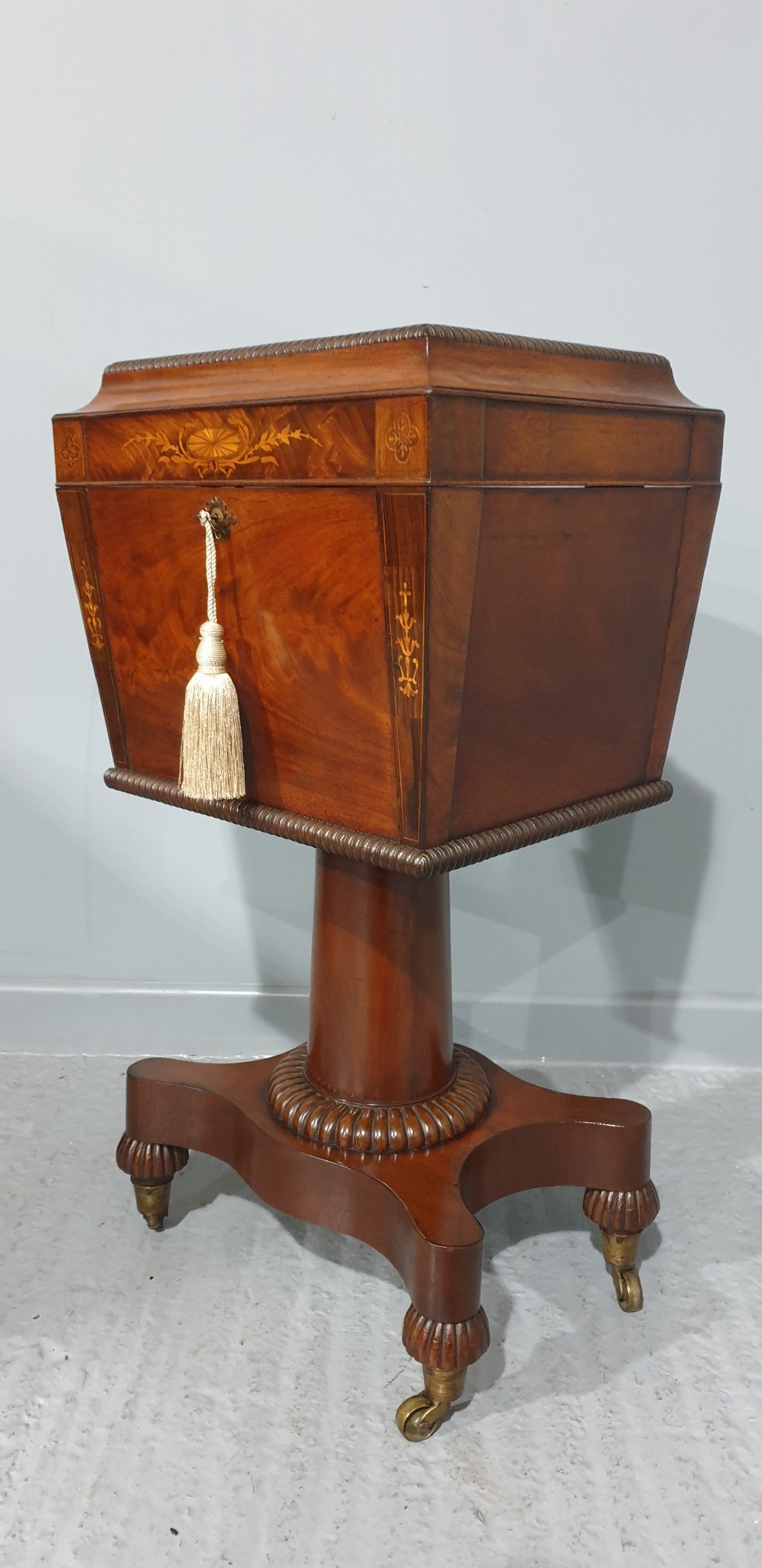 A William IV mahogany pedestal wine cellarette with marquetry inlay, gadrooned trim, and a quadform base on brass castors. View V